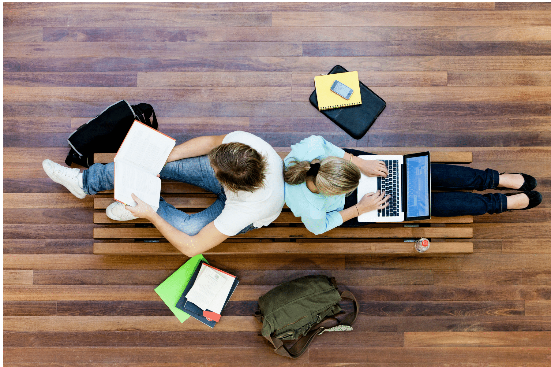 photo taken from above of two people sitting back to back on their laptops